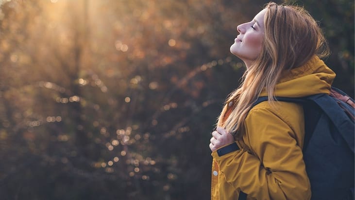 woman standing in nature and breathing fresh air and taking a self-care