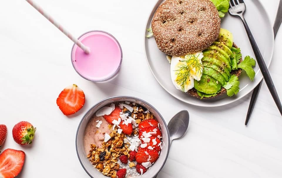 Food on the table. An oatmeal bowl with strawberries, plate with avocado toast and pink fruit smoothie.