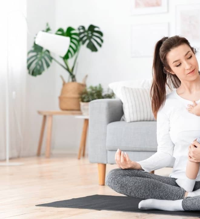 Mom is holding her baby son while siting in lotus pose and meditating.