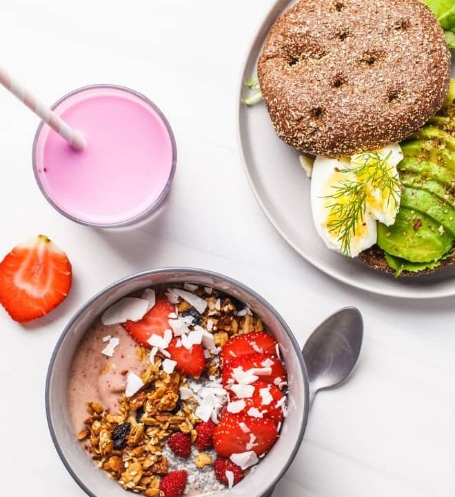 Food on the table. An oatmeal bowl with strawberries, plate with avocado toast and pink fruit smoothie.