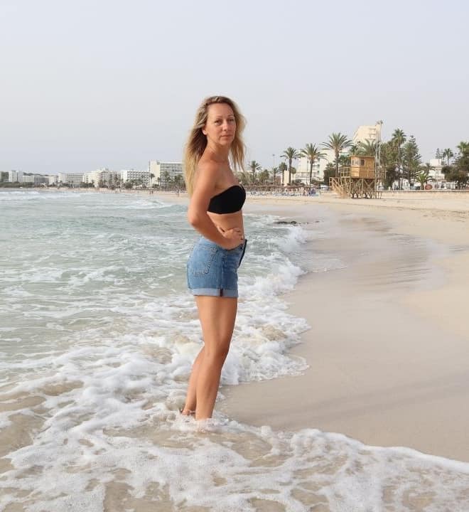 Pilates Instructor standing in a top and leggings on the beach. Wearing beautiful Women's best active wear set.